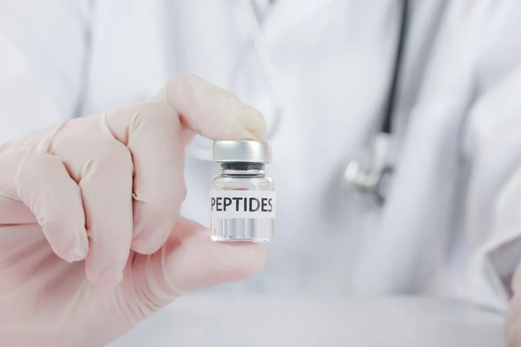 Clinician in gloves holding a vial labeled Peptides